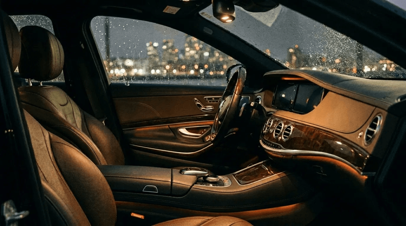 Interior of a chauffeured luxury sedan at night, city lights through rain-flecked windows